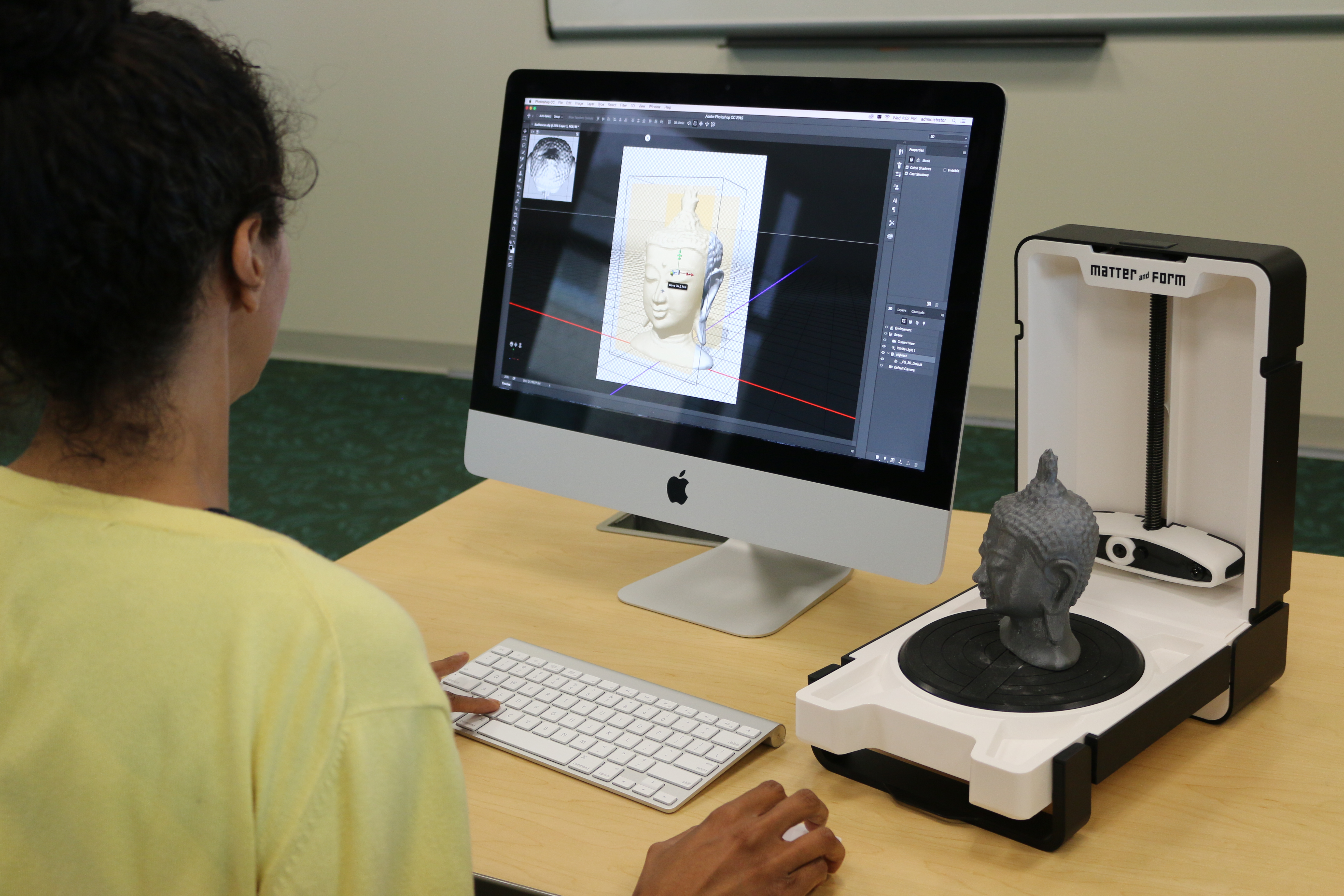 Young woman, back turned, working on a computer with a 3D scanner.