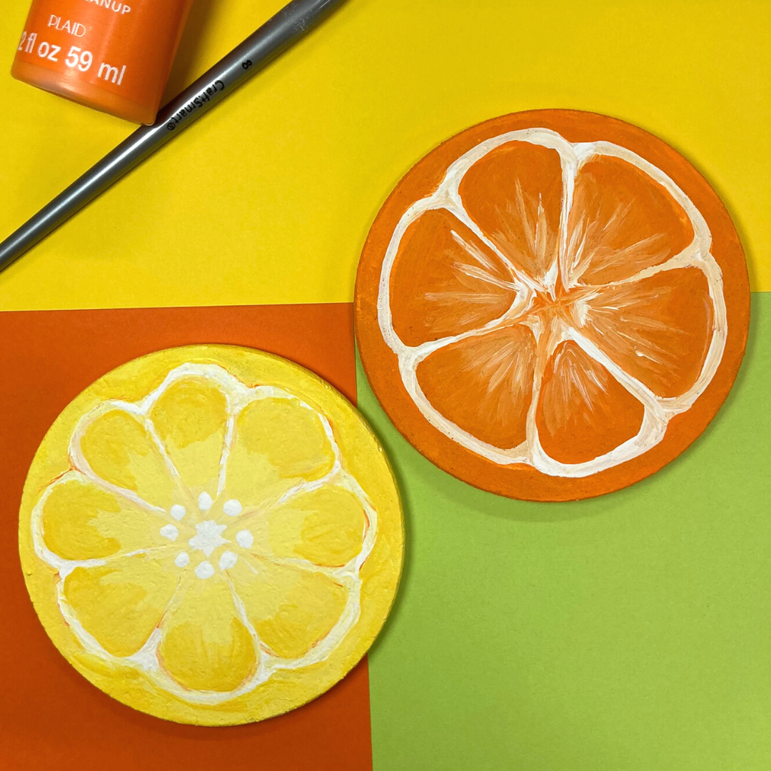 Two round coasters, one painted to be a lemon slice and the other an orange slice.