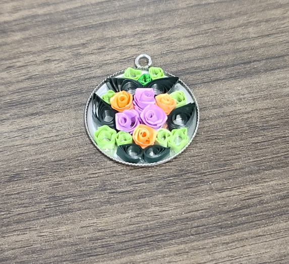 A circular pendant decorated with twirled paper flowers. 