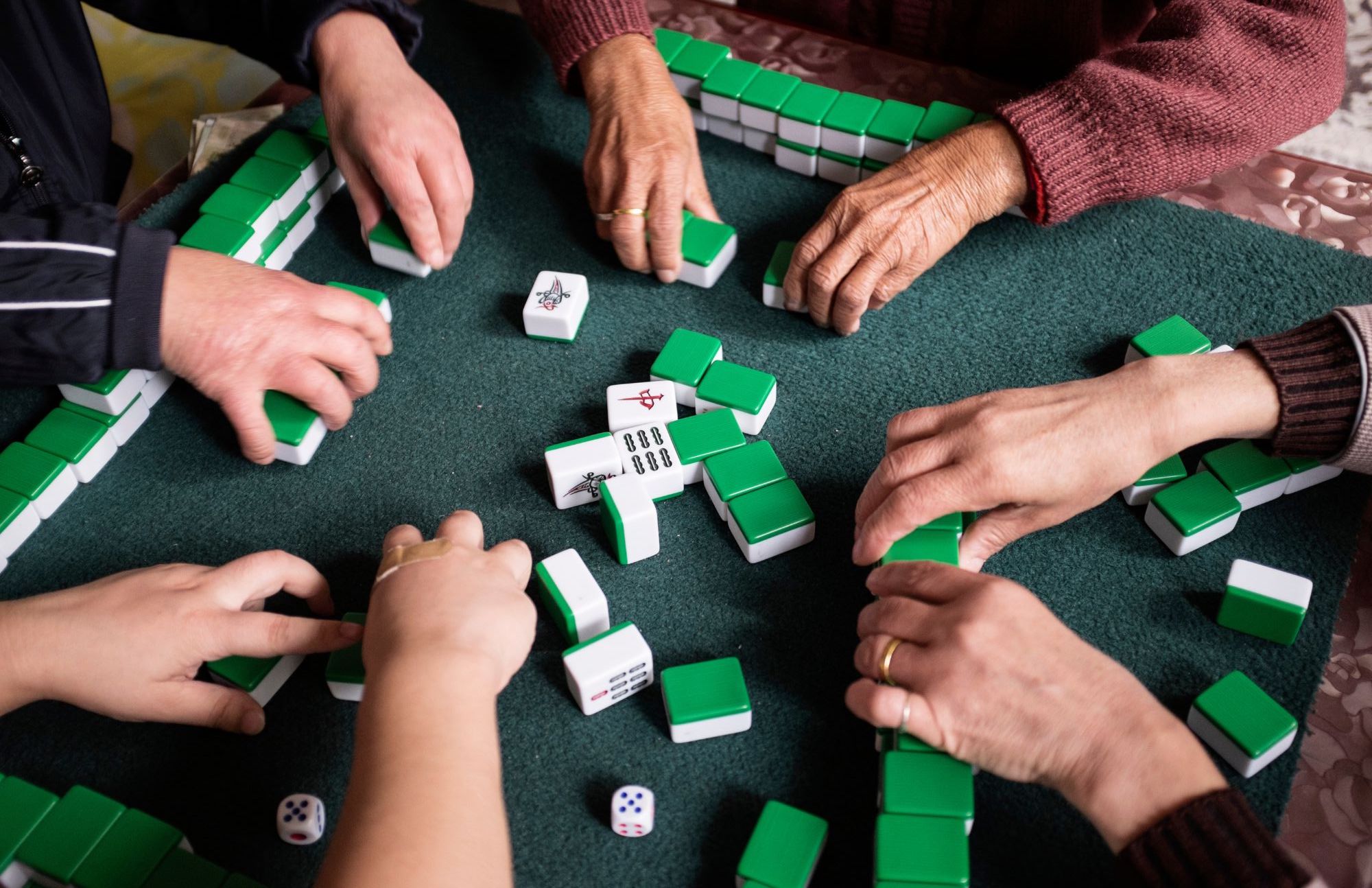 image depicts multiple people playing mahjong and picking up tiles