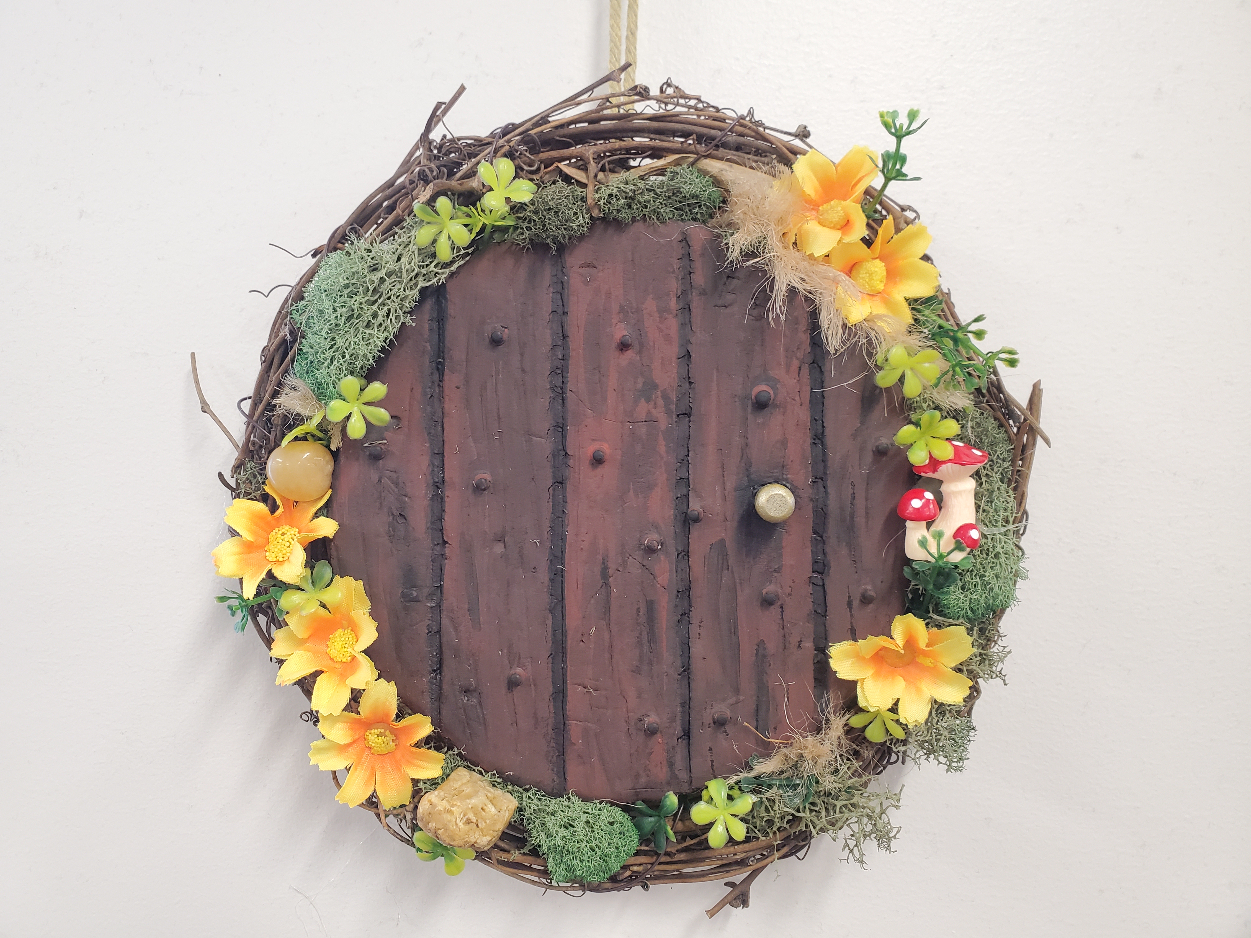 wreath made to look like door with flowers, moss, and rocks around it
