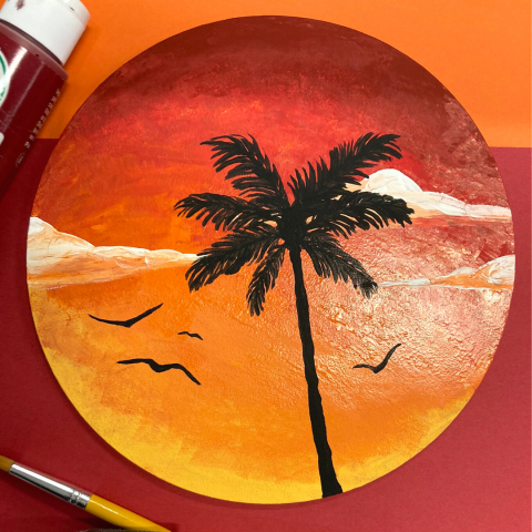 An 8" wooden disc painted with a sunset and the silhouette of a palm tree and four seagulls.