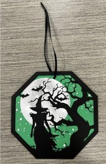 Image of octagon ornament featuring a witch against a green background with a moon, bats, and tree behind her