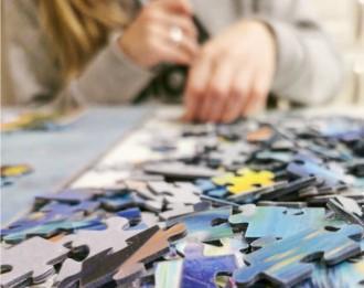 Image of jigsaw puzzle pieces in the foreground and a person solving the puzzle in the background