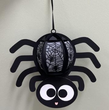 Picture of a paper spider lantern hanging from a black thread against the wall.