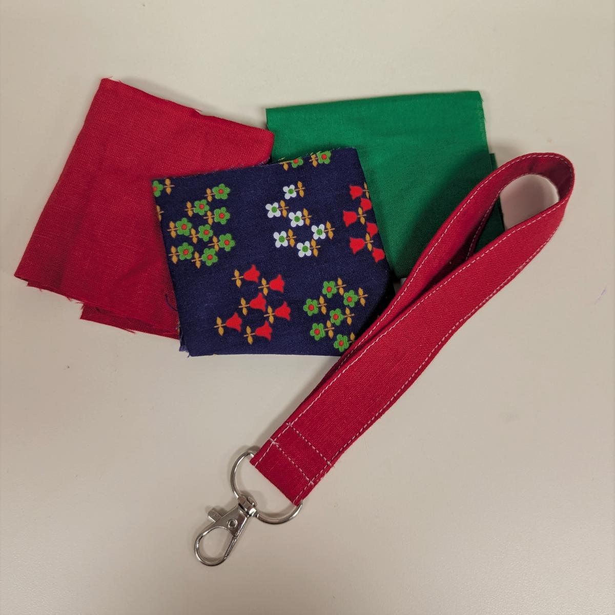 Photo of sample red wrist lanyard and fabric swatches in green, red, and a purple floral pattern.